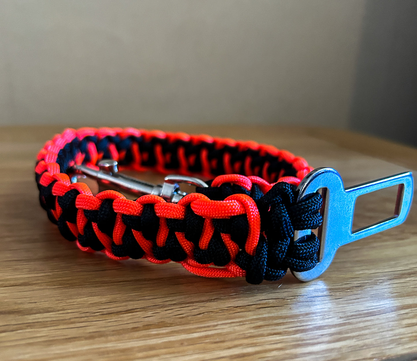 Paracord dog seatbelt clip with red and black pattern on a wooden surface