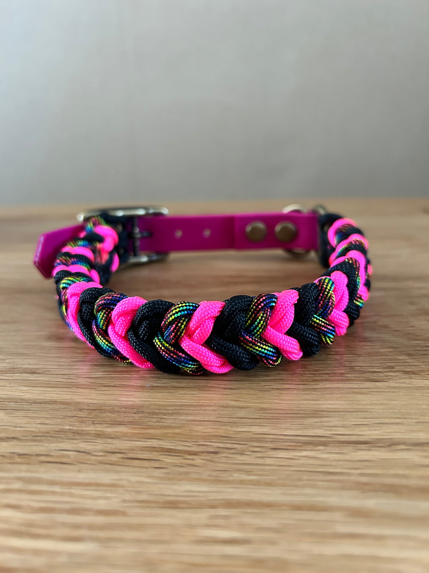 Paracord dog collar with pink and black design on a wooden surface