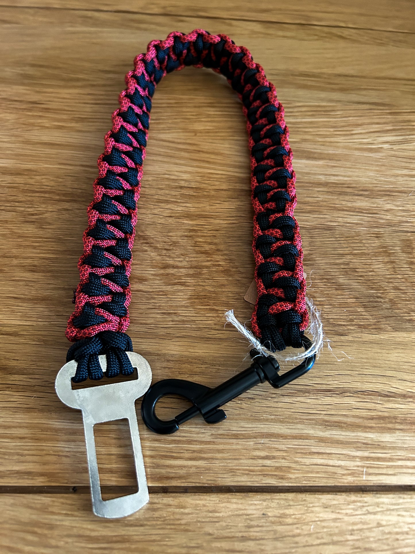 Red and black braided seatbelt clip for dogs with carabiner on a wooden surface