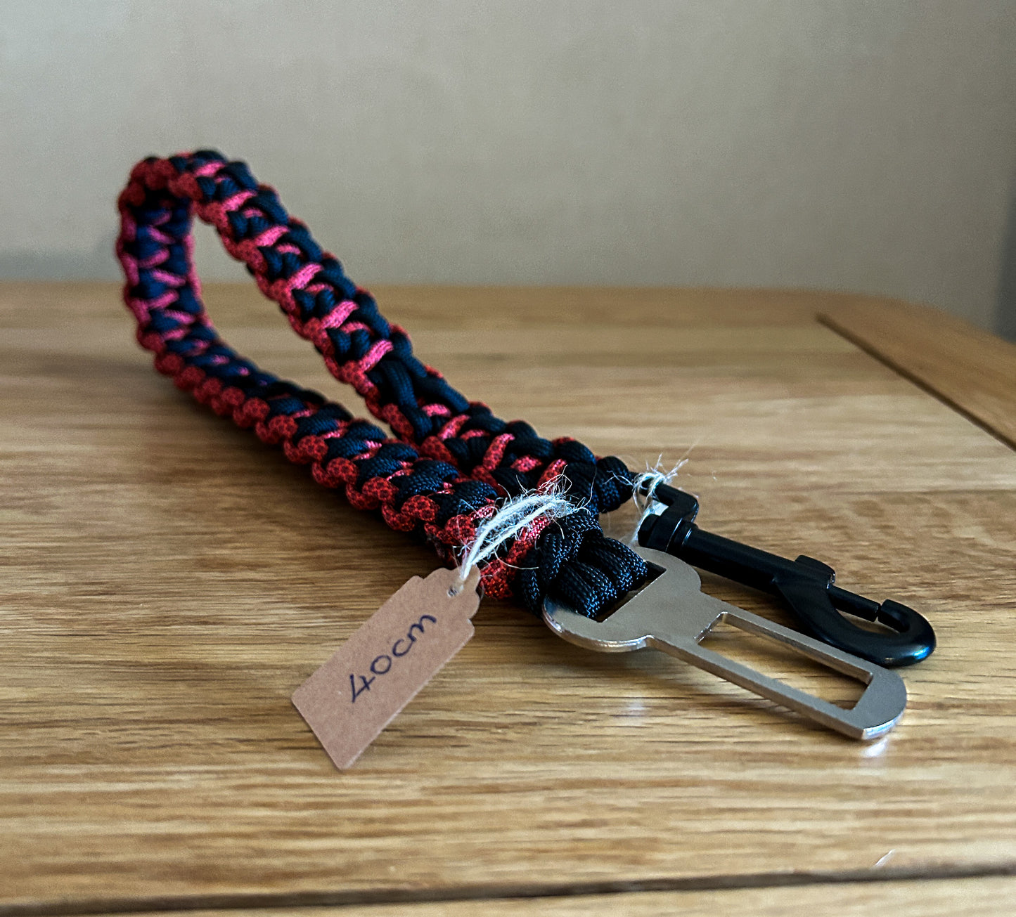 Paracord seatbelt clip with red and black pattern on a wooden surface