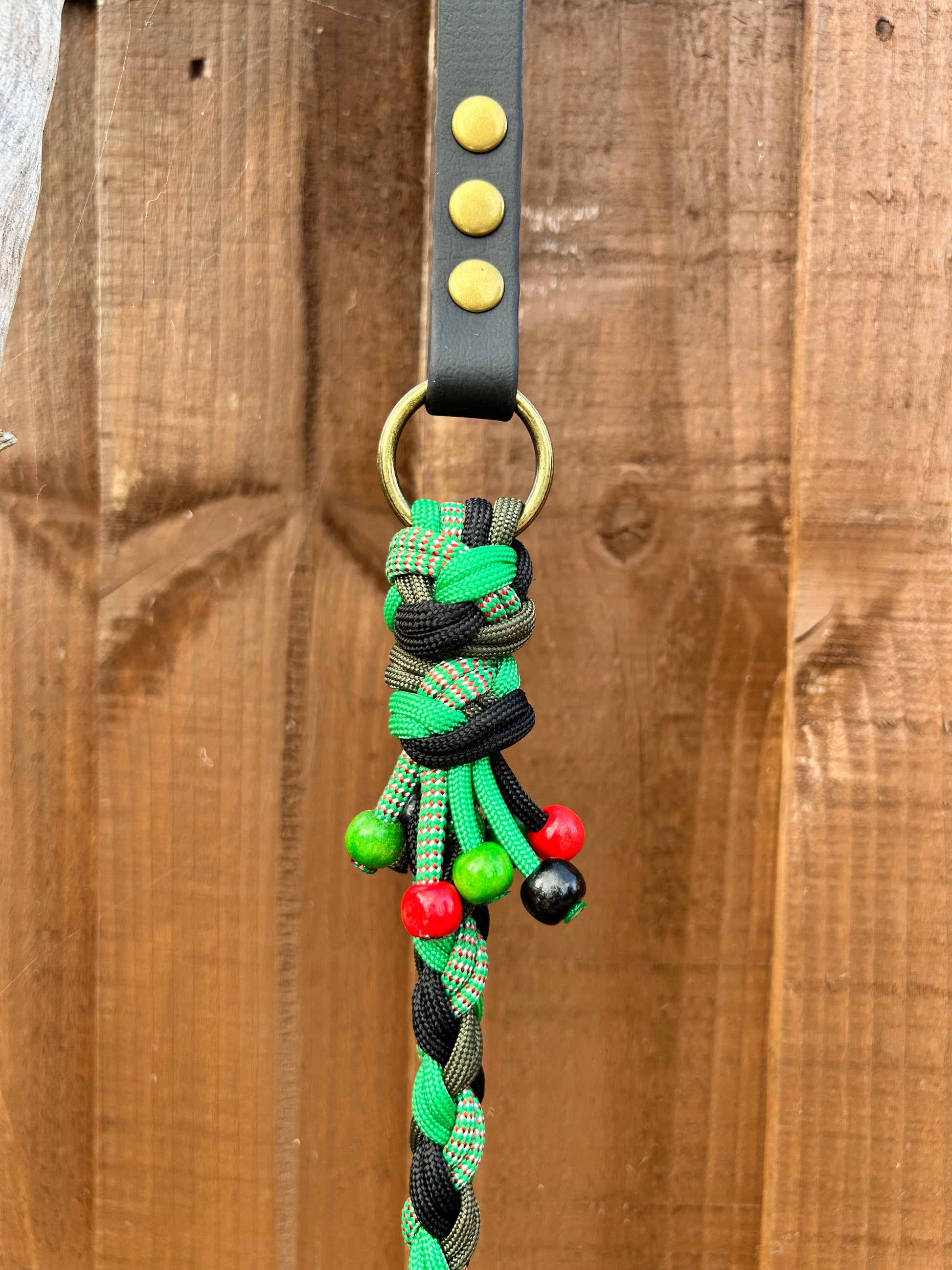 Dog leash with green and black braided design and red and black beads on a wooden surface