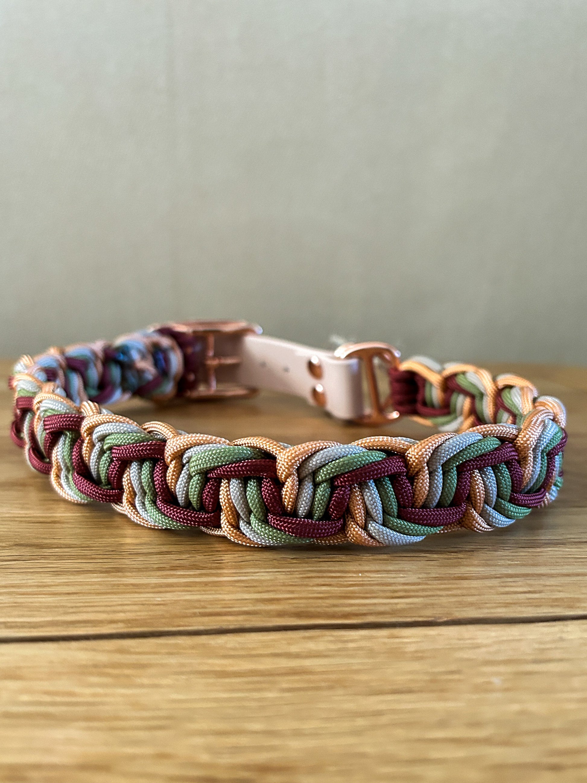 Multicolored braided dog collar on a wooden surface with a neutral background